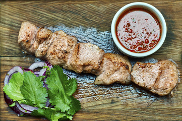 Pieces of barbecue with tomato sauce and parsley leafs with onion rings on wooden board