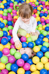 Fototapeta na wymiar Two children play fun in colorful balls and one girl lays balls on another