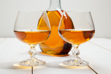 Glasses with cognac and a bottle on  white wooden background
