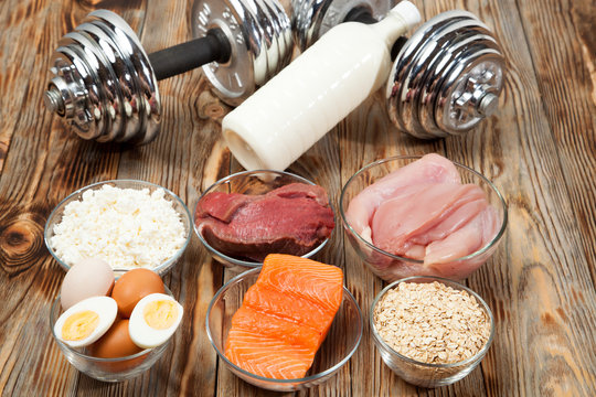 Protein, Fish, Cheese, Eggs, Meat, Chicken And Dumbbells On A Wooden Background