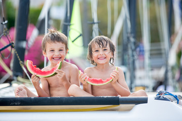 Two little children, boy brothers, eating watermelon on the beach