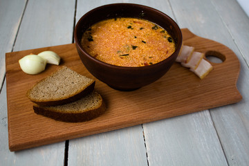 bowl of red soup bread onion on board