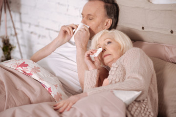 Senior couple blowing noses on bed