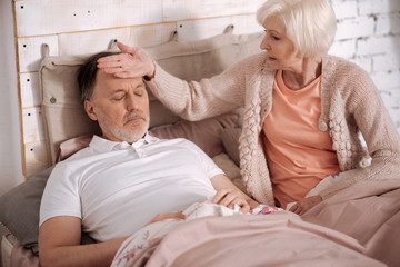 Obraz premium Senior lady feeling temperature of her sick husabnd