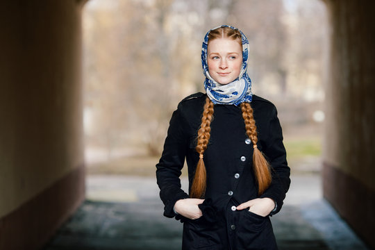 Young beautiful fashionable redhead woman with braids hairdo in blue white headcraft stylish denim black trench jacket posing outdoors in street arc spring time