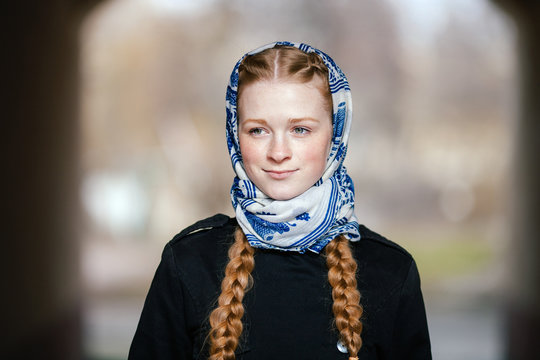 Young beautiful fashionable redhead woman with braids hairdo in blue white headcraft stylish denim black trench jacket posing outdoors in street arc spring time