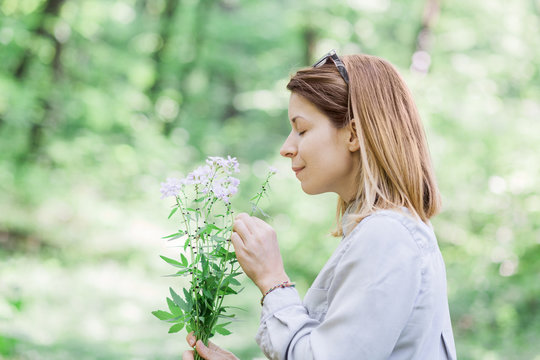 Young Woman Smelling Flowers Outside In Nature