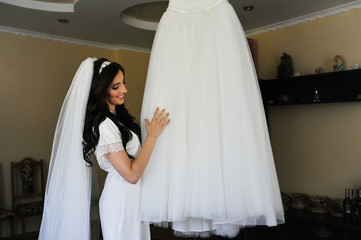 Beautiful brunette bride at morning gown with wedding dress at room.