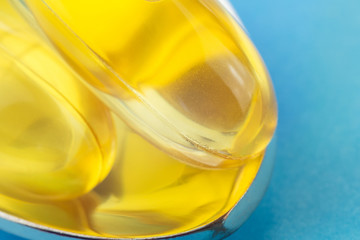 Two yellow capsules of omega 3, fatty acid, fish oil in the spoon, on blue background, macro image.