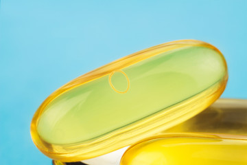 Yellow capsules of omega 3, fatty acid, fish oil on blue background, macro image.