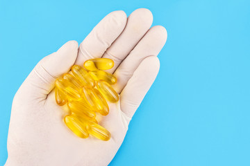 Hand in medical glove keeps lot of yellow capsules omega 3, fatty acid, fish oil on blue background.