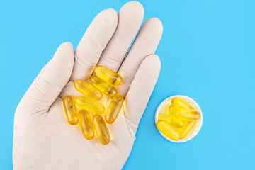 Hand in medical glove keeps lot of yellow capsules omega 3, fatty acid, fish oil on blue background.