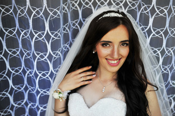Beautiful smiling brunette bride at wedding dress near window at room on tulle curtains.