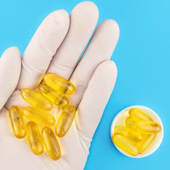 Hand in medical glove keeps lot of yellow capsules omega 3, fatty acid, fish oil on blue background.