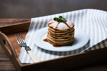 American pancakes on a plate with mint and caramel syrop. Dark background. Setted on a wooden tray with a fork