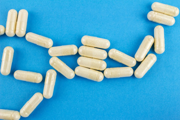 White capsules of glucosamine chondroitin, healthy supplement, pills on blue background, top view, macro image.