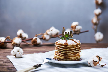 Obraz na płótnie Canvas American pancakes on a plate with mint, caramel, syrup, love sign and sugar powder. With the cotton branch on a back and a copy space.