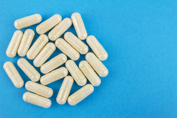 White capsules of glucosamine chondroitin, healthy supplement, pills on blue background, top view, macro image.