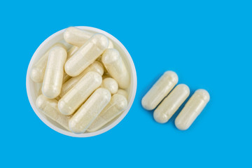 White capsules of glucosamine chondroitin, healthy supplements, pills in round bottle, on blue background, top view.