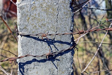 Колючая проволока на сером бетонном столбе