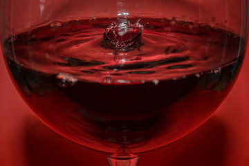Rotwein Tropfen in einem Rotweinglas und Wellen mit rotem Hintergrund und Spiegelung