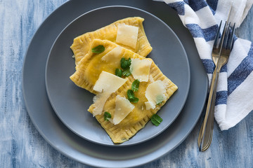 Homemade ravioli with spinach and ricotta cheese with grated parmesan on blue plate. Selective focus