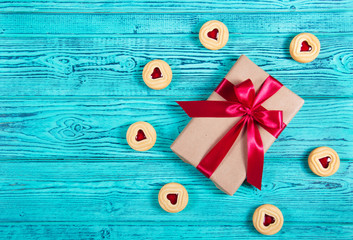 Gift box with satin bow and cookies with marmalade in the shape of heart. A romantic gift. Present on a turquoise background. Copy space. Flat lay