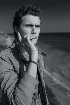 Young man smoking cannabis on the sea background. Black and white
