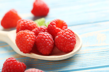 Red raspberries in spoon on a blue wooden table
