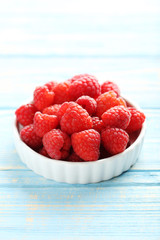 Red raspberries in bowl on a blue wooden table