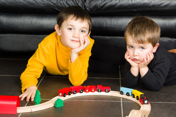 Children playing with wooden toy train. 2 little boys build wooden railroad at home lying on the floor