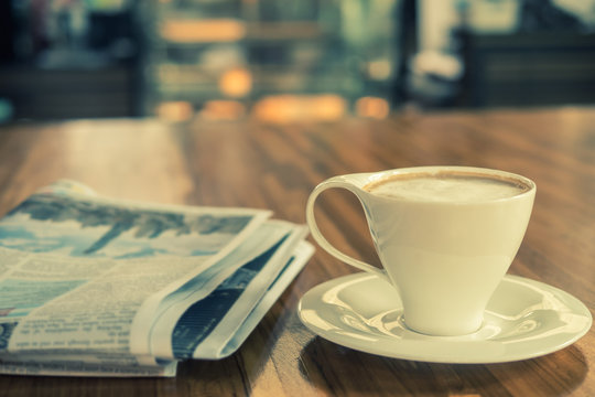 Cup of cappuccino with newspaper on the table in in the morning at coffee shop , warm tone