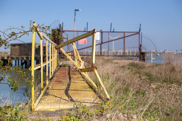 Damaged footbridge front of an abandoned rusted gate with razor wire on a seaside bridge at Isle of Sheppey England United-Kingdom 