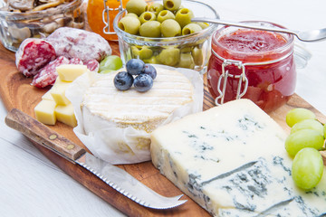 wooden cutting board with cheese, cold cuts and jams