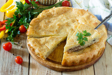 A classic quiche Lorraine pie with potatoes, cabbage, fish and cheese on a wooden table.