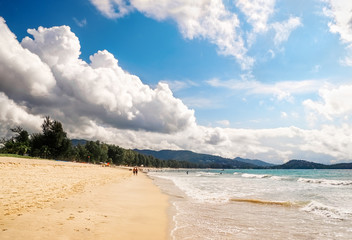 Tropical beach scenery at Andaman sea in Phuket, Thailand. Exotic sea view with people relaxing on vacation at tropical summer paradise beach of Phuket island with sunny sky and clouds on horizon