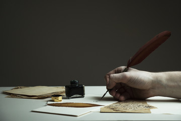 Scene with a man's hand writing a letter or story with vintage quill and old pieces of paper on...