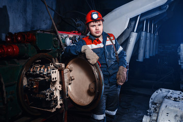 Fototapeta na wymiar young coal miner is underground in a mine for coal mining in overalls against the backdrop of mining equipment. concept of repair of industrial equipment.