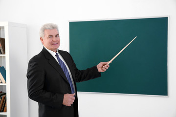 Senior teacher with pointer standing near blackboard