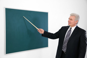 Senior teacher with pointer standing near blackboard