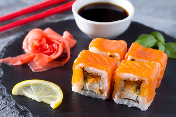 Roll Jamaica on a black slate board - tobiko orange salmon, salmon, soft cheese, cucumber, nori, rice.
