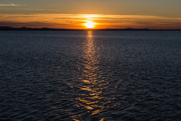 Sunset at the lake, with the sun low on the horizon and a very long reflection on dark water