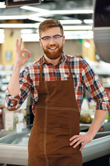 Cheerful cashier man on workspace in supermarket shop.
