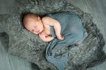 Newborn baby boy swaddled laying on fur