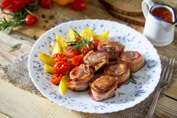 Pork fillet baked in bacon and baked potatoes, fresh vegetables and herbs on a wooden table in a rustic style.