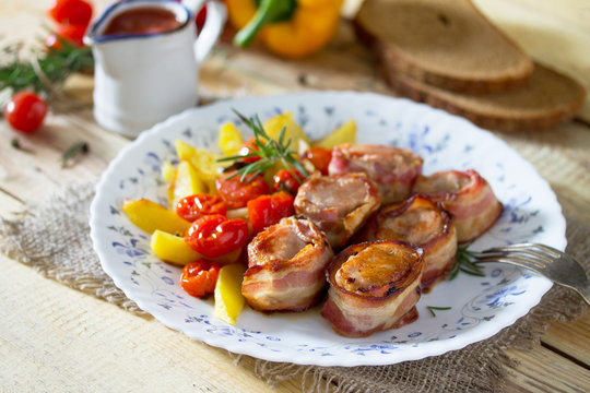 Pork fillet baked in bacon and baked potatoes, fresh vegetables and herbs on a wooden table in a rustic style.