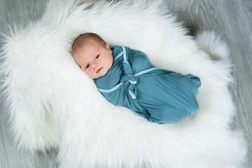 Newborn baby boy swaddled and laying on fur