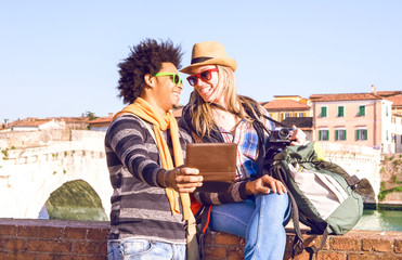 Interracial couple of friends travelers taking selfie in old town riverside at sunset - Happy young tourists looking at each other having fun moment with self romantic photo on city background