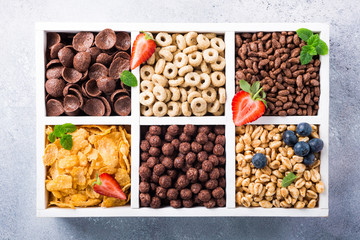 Variety of cold quick breakfast cereals with berries in white wooden box, healthy eating for kids, overhead shot