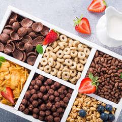 Variety of cold quick breakfast cereals with berries in white wooden box, healthy eating for kids, overhead shot